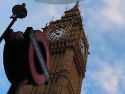 Colorful "Underground" sign and beautiful Big Ben clock on the tower in London, England, under the blue sky with white clouds