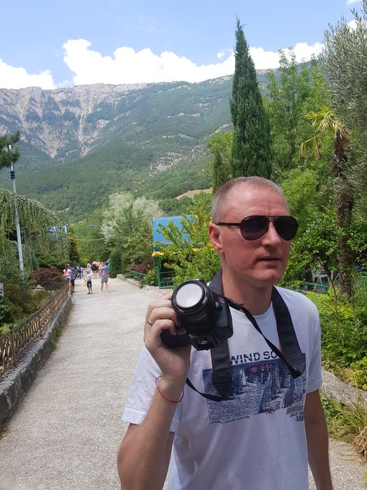 Walking man with the camera and sunglasses among the plants