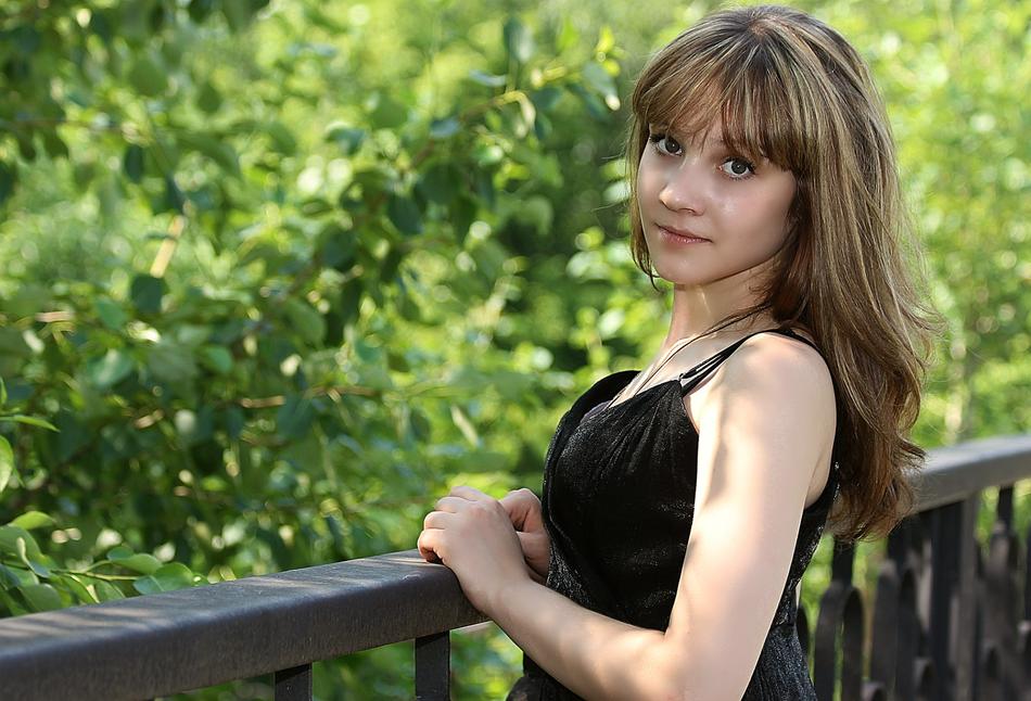 Beautiful girl in black dress, posing on the railing of the bridge, near the beautiful, green plants