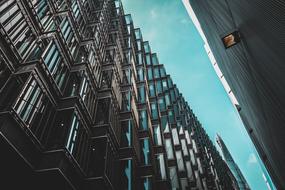 Low angle shot of the shiny building with the windows, under the turquoise sky with the clouds