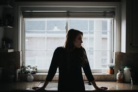 the girl stands near the table and the window