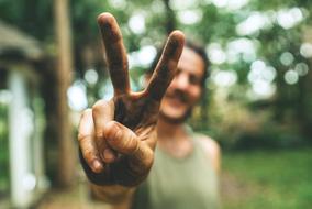 Smiling man, showing peace sign, among the green plants