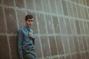 teenager with glasses near a stone wall