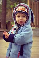 Portrait of the boy, covered in colorful clothes, near the building and plants