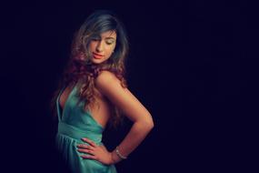 Girl in turquoise dress, with the curly hair and bracelet, in light, among the darkness