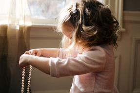 Cute child girl with the curly hair, with the necklace in the hand