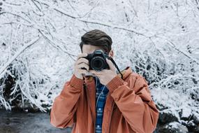 Man photographer with the camera near the beautiful snowy trees in winter