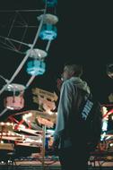 young Man Smoking cigarette near ferris wheel in amusement park at night