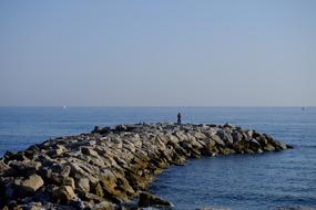 Man, fishing on the beautiful, rocky shore of the sea, at blue sky on background