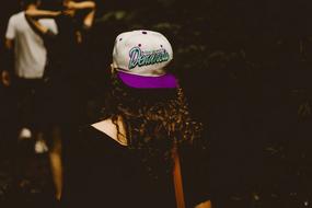Back view of the girl with curly hair, in the colorful cap, at the night