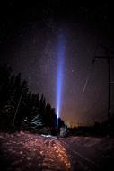 man shines a flashlight into the starry sky