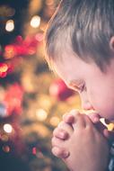 Profile portrait of the praying boy, at background with the colorful and beautiful bokeh lights