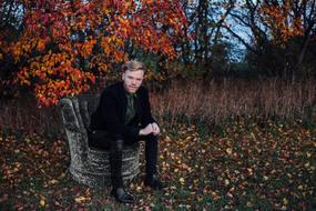 young Man sits beneath tree at fall