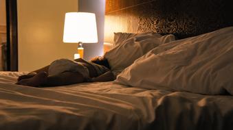 child on a large bed near a table lamp