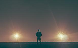 Silhouette of the guy, standing on the meadow in lights, in the evening