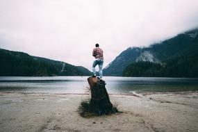 photo of a man on a high stump by the lake