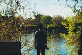 Back view of the guy with the camera, near the beautiful river, among the colorful plants, in the fall