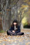 Girl sitting on the path with the colorful and beautiful leaves, among the colorful and beautiful trees in the late autumn