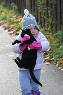 girl carries a black kitten in her arms