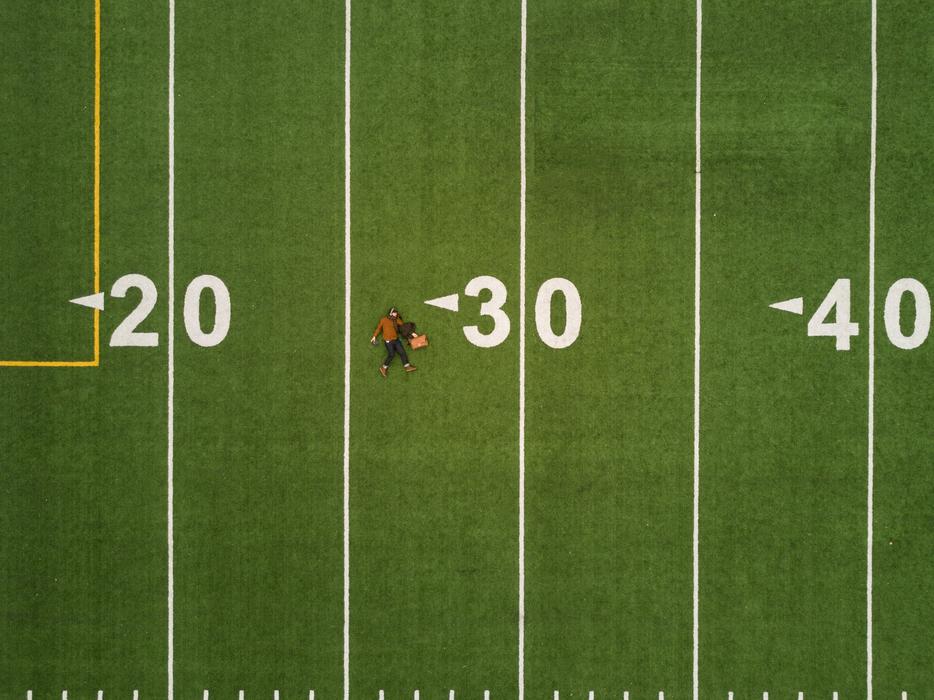 Man, laying on the green grass field with the white and yellow numbers