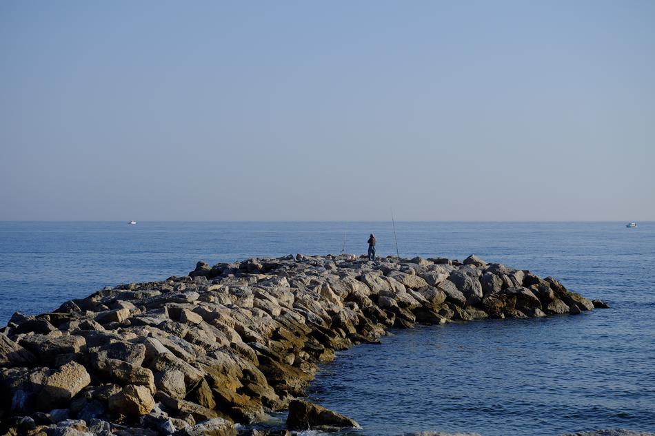 Man, fishing on the beautiful, rocky shore of the sea, at blue sky on background