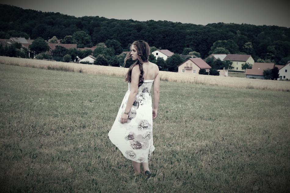 Black and white photo of the beautiful girl in dress, on the beautiful field near the houses, in the village