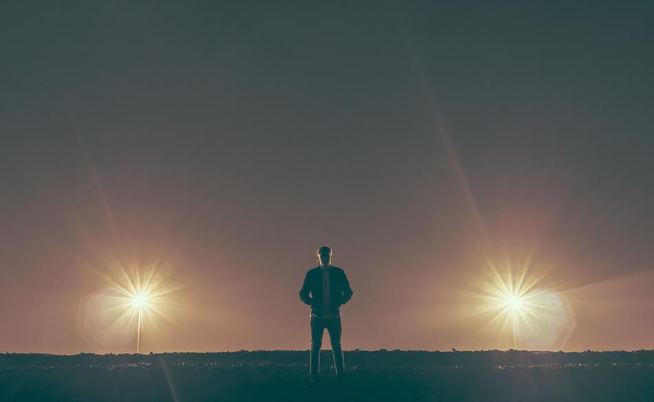 Silhouette of the guy, standing on the meadow in lights, in the evening