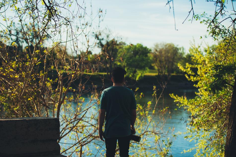 Back view of the guy with the camera, near the beautiful river, among the colorful plants, in the fall