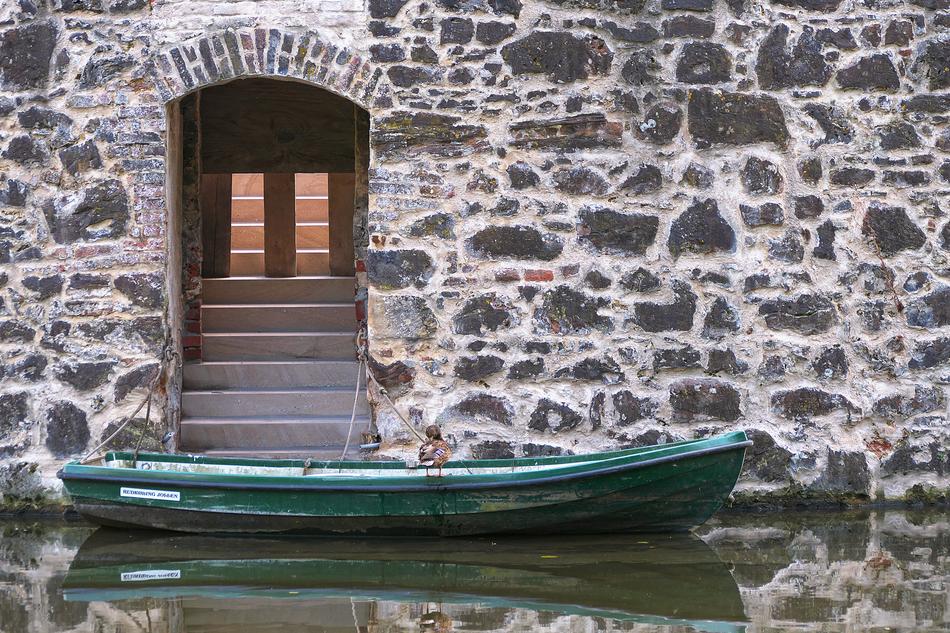 Green boat in the moat near the stone wall of the castle, in Wasserburg, Germany