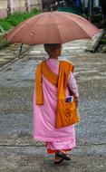 Colorful, young girl monk, with the umbrella, walking on the path in Yangon, Myanmar