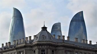 Shiny, glass buildings behind the beautiful, old architecture, under the sky with clouds