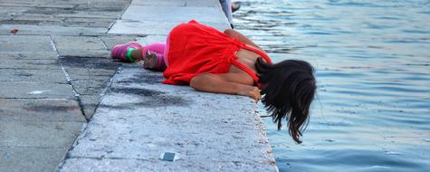 little girl in red bent over the water