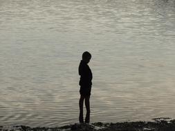 silhouette of a boy standing by the lake