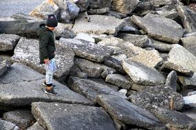 Child in hat, walking on the pieces of the stones, on the beach