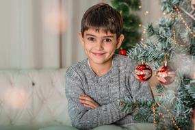 child boy sits at Christmas tree