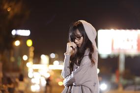 Beautiful girl with the glasses and hood, on the street with the colorful lights, at the night