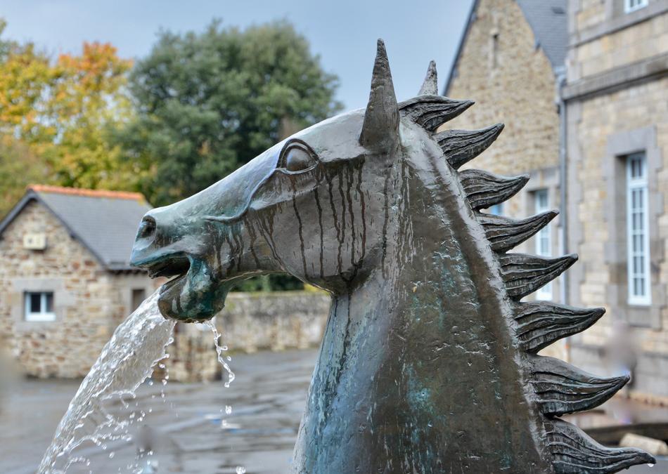 Profile view of the horse statue with water fountain, on the beautiful landscape with buildings and plants in Lamballe, Brittany, France