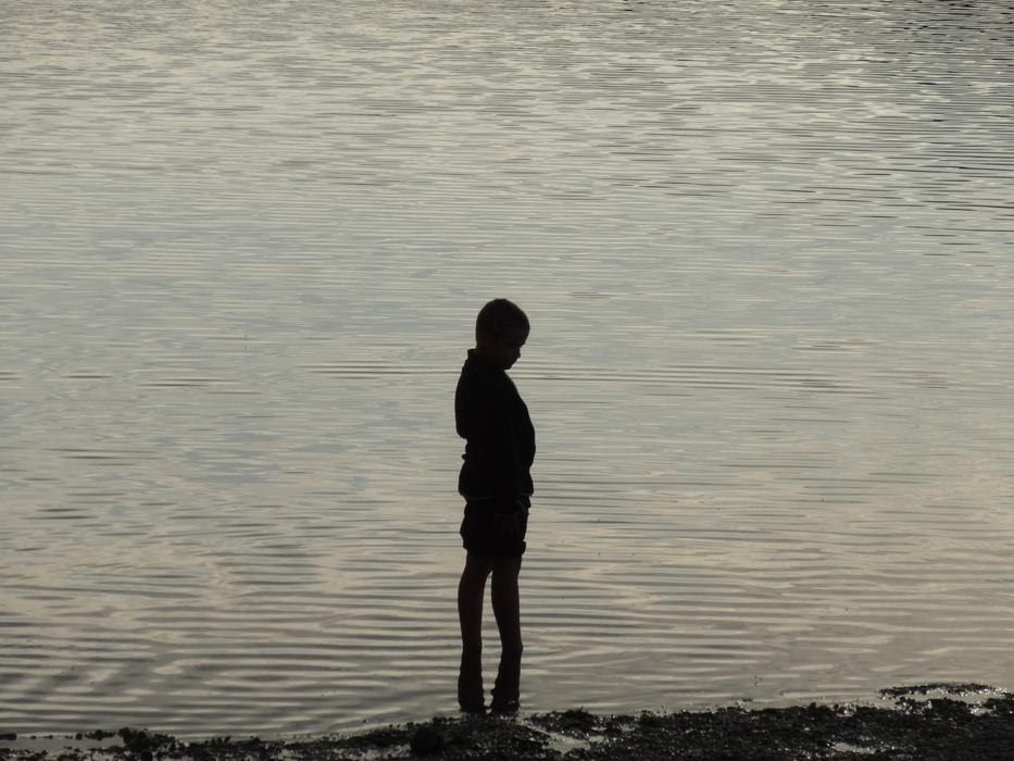 silhouette of a boy standing by the lake