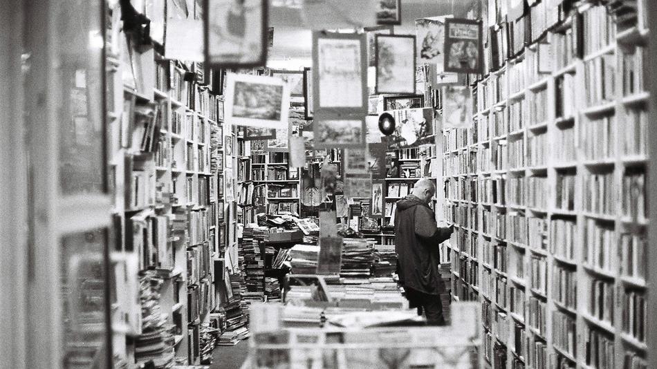 Black and white photo with the man, among the books and paintings