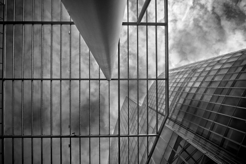 Black and white photo with low angle shot of the glass building, under the sky with clouds, in DÃ¼sseldorf, Germany