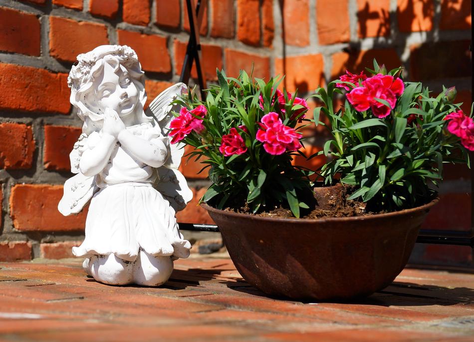 Beautiful still life with the white figure of angel near the pot with red flowers