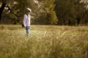 Photo of the girl, walking on the colorful field with the grass, near the trees, on the photo with sepia effect