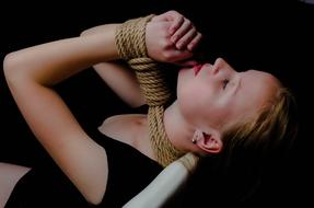 Blonde girl in shibari ropes, in light, among the darkness