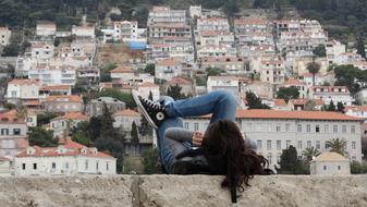 Girl in jeans relaxing on stone wall in front of old city, croatia, dubrovnik