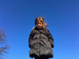 Smiling girl in black jacket, near the trees, under the blue sky