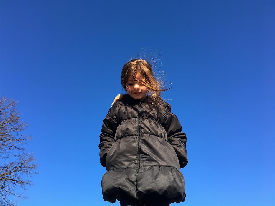 Smiling girl in black jacket, near the trees, under the blue sky