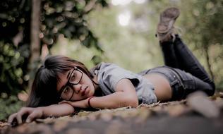 Indonesian girl with glasses, laying on the path, among the green plants