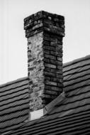 Black and white photo of the old, stone chimney on the roof of the house