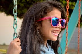 Smiling, cute girl, with the colorful sunglasses, on the swing