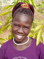 Portrait of the smiling girl, near the colorful plants, on the mission in South Sudan